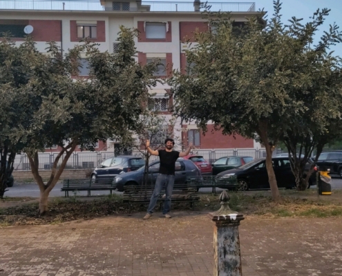 Gabriele Primavera raising his hands among a couple of carob trees he planted himself in a public square in Latina (Italy)